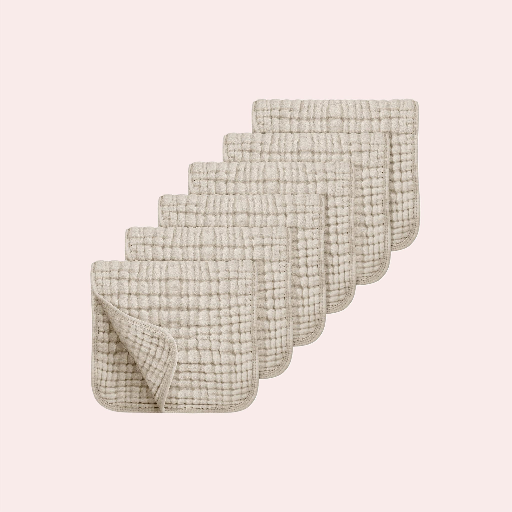 Six 100% cotton muslin baby burp cloths with quilted grid texture, stacked on a pink backdrop.