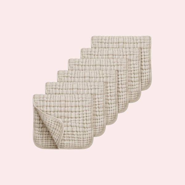 Six 100% cotton muslin baby burp cloths with quilted grid texture, stacked on a pink backdrop.