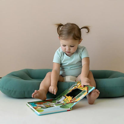 Child playing happily beside a green baby lounger cushion